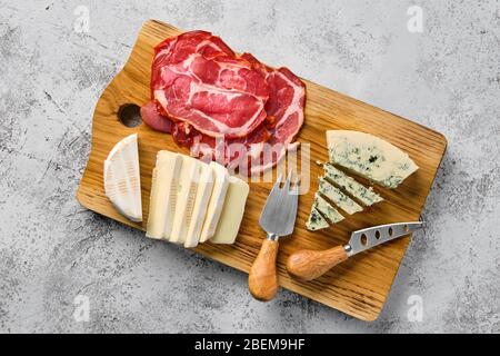 Top view of wooden cutting board with smoked bacon, brie cheese and gorgonzola Stock Photo
