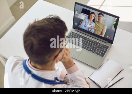 Doctor medical online call.Shoulder view doctor therapist psychologist speaks with couple video chat using a laptop in a clinic office. Stock Photo