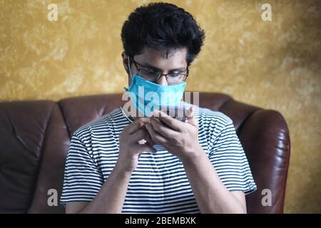 man using smartphone while wearing surgical mask indoor . Stock Photo