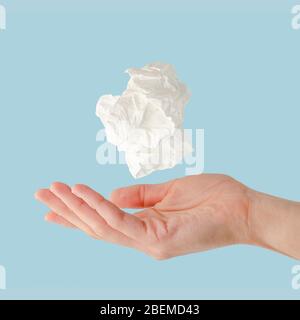Crumpled handkerchief flying over female hand on blue background, Health care and colds concept. Stock Photo
