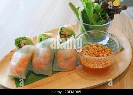 Fresh vegetables and prawn spring rolls served with green salad on a wooden plate Stock Photo