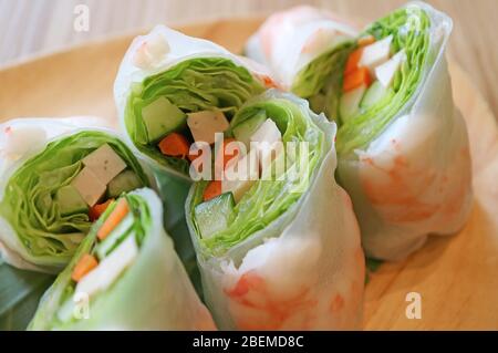 Closeup delectable fresh vegetables with prawn spring rolls on a wooden plate Stock Photo