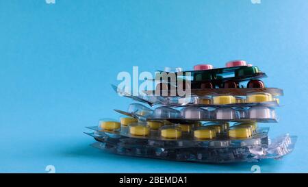 Packs of pills of various shapes and colors are stacked on a blue background. Capsules are packaged in blister packs. Different medicines. Drug treatm Stock Photo