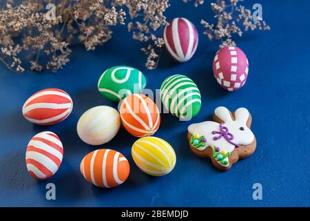 Attributes of the chrestian Easter holiday - colored eggs and gingerbread in the form of a rabbit on a dark blue background. Contrast Stock Photo
