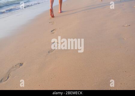 Sea vacation. someone walking on the beach. Beach travel, man walking on sand beach leaving footprints in the sand. Closeup detail of male feet and Stock Photo
