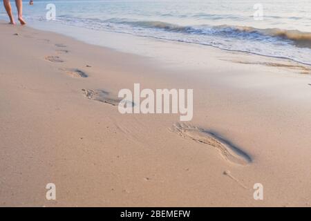 Sea vacation. someone walking on the beach. Beach travel, man walking on sand beach leaving footprints in the sand. Closeup detail of male feet and Stock Photo