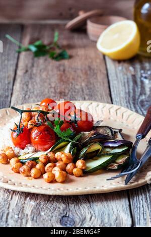 Vegan plant based dish, bowl with quinoa, chickpeas, grilled courgette, eggplant, tomatoes in ceramic bowl on rustic wooden table, sustainable lifesyl Stock Photo