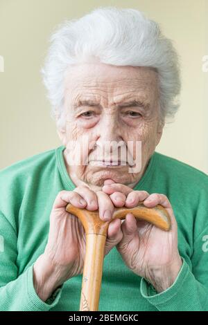 closeup of a sad old woman leaning on a wooden cane Stock Photo