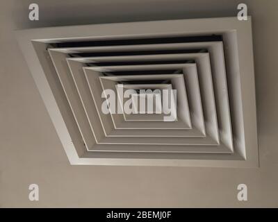 Photo at an angle of a ventilation hatch with a cover with a square pattern hanging on a light ceiling Stock Photo