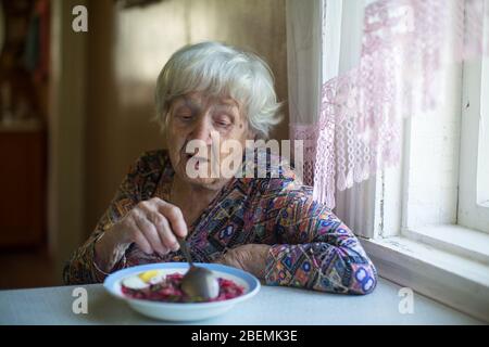 An Old woman eating soup sitting at a table in the her house. Stock Photo