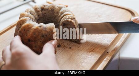 Closeup view of female hand cutting freshly baked vegan banana bread with chocolate and pecans. Stock Photo