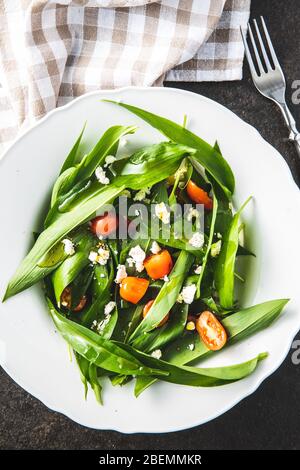 Fresh salad with wild garlic,tomatoes and feta cheese on plate. Ramsons leaves. Top view. Stock Photo