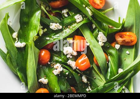 Fresh salad with wild garlic,tomatoes and feta cheese on plate. Ramsons leaves. Stock Photo
