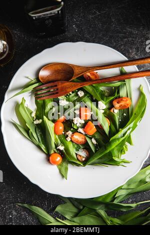 Fresh salad with wild garlic,tomatoes and feta cheese on plate. Ramsons leaves. Top view. Stock Photo