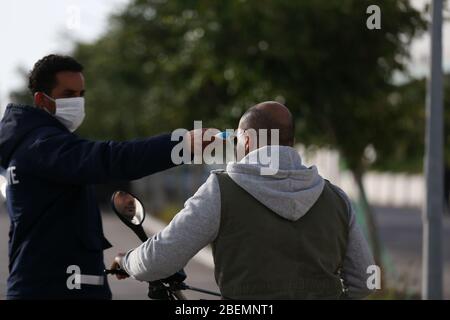 Manouba, Tunisia. 14th Apr, 2020. A security guard measures the temperature of a worker on Apr. 14, 2020 in Industrial Zone Agba, Manouba, Tunisia. After the announcement of total containment throughout Tunisia on March 22, 2020, factories and viral sectors are continuing their activities while respecting the precautions against the pandemic of CoViD-19. This story follows the daily routine of workers at Marquardt Tunisia automotive factory in Manouba, Tunisia during the Covid-19 coronavirus pandemic. (Photo by Mohamed Krit/Sipa USA) Credit: Sipa USA/Alamy Live News Stock Photo