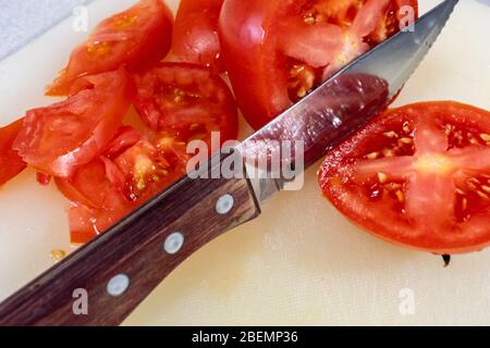A steak knife with a wooden handle slices through a red beefsteak tomato on a cutting board. Stock Photo
