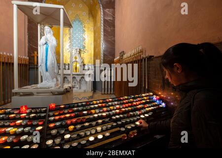 Woman praying to Virgin Mary statue after lighting a candle at the Basilica of our Lady of the Rosary in the Sanctuary of Our Lady of Lourdes, France Stock Photo