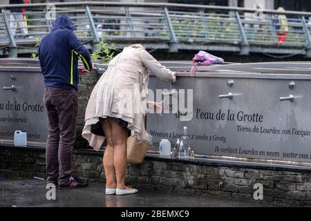 Pilgrims collecting holy water from faucets at the sanctuary in Lourdes, France, Europe Stock Photo