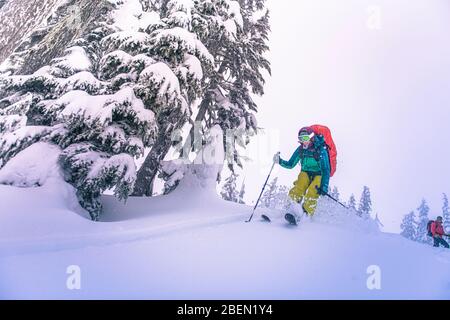 Woman jumping from top of snowy hill while backcountry skiing in BC Stock Photo