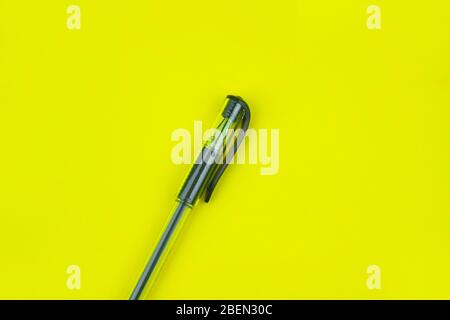 Black colored ball point pen placed over a bright yellow colored empty paper background Stock Photo