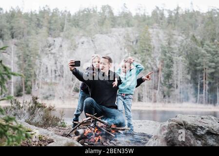 father taking selfies with his kids whilst sitting next to a campfire Stock Photo