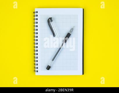 Open ball point pen of black color placed on top of a white paper diary on a yellow paper background Stock Photo