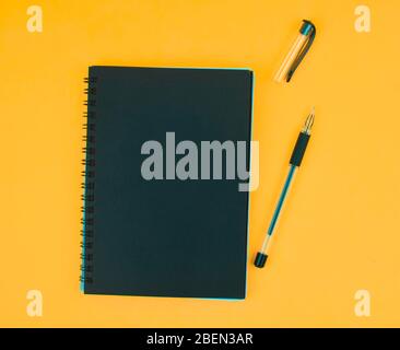 Opened black colored ball point pen placed beside a black colored paper diary on an orange paper background Stock Photo