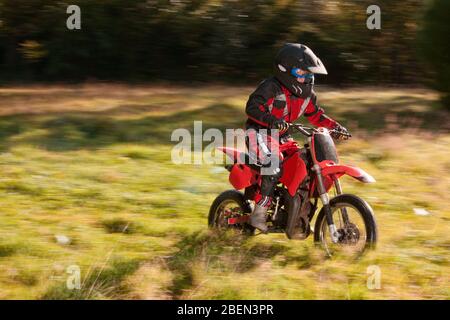 12 year old boy riding his motocross motorcycle through field