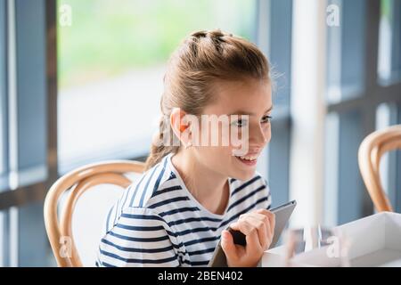 A portrait of a girl with braided hair, who is sitting on a chair with a gadget and looking at something. Stock Photo