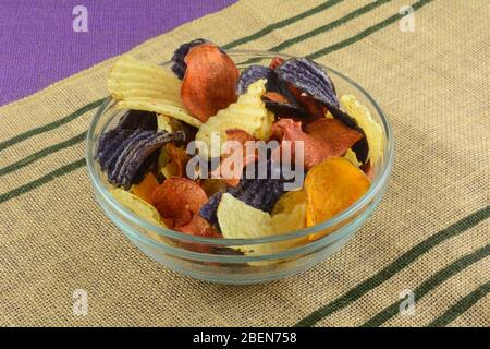 Vegetable chips made from yukon gold potatoes, blue potatoes, and sweet potatoes in glass snack bowl on place mat Stock Photo