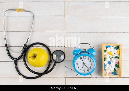 Time to accept tablets. Phonendoscope and tablets in a wooden box along with a blue watch on a white wooden table Stock Photo