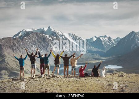 Big group of happy young hikers are standing with raised arms in mountains Stock Photo