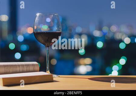 A glass of red wine on wooden table when reading book with colorful bokeh lights. Stay home concept. Stock Photo