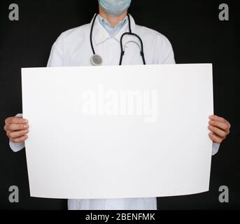 A man in a black t-shirt and medical gloves holds a white sheet of paper. Mockup. Coronavirus. Quarantine . Epidemic. Copy space. Warning. Doctor's hand in blue glove holding sheets of paper. Stock Photo