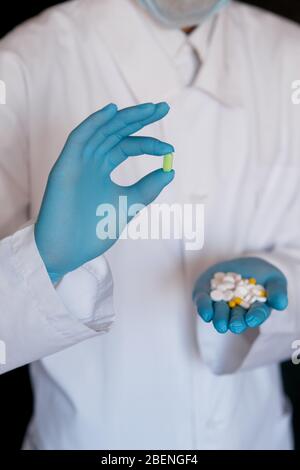 Many small white pills in the hands of a doctor wearing medical blue disposable gloves. Hands take one pills. Stock Photo