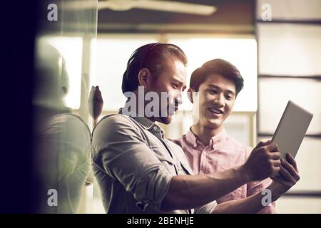 two asian businessmen working together in office looking at digital tablet Stock Photo