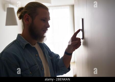 Young man using smart home thermostat technology device on wall. Stock Photo