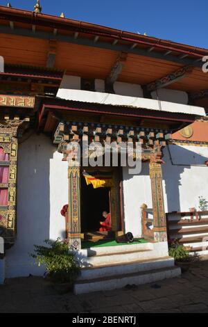 A young monk sits in the entrance doorway of Chimi Lhakhang, or fertility temple, near Punakha, Bhutan, which dates from 1499. Stock Photo