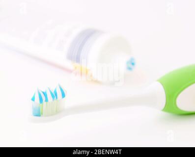 Toothbrush head with toothpaste and toothpaste tube on white background. Focused on foreground. Shallow depth of field Stock Photo