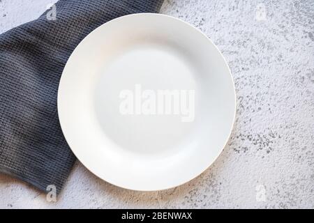 Empty white plate next to a gray kitchen towel Stock Photo