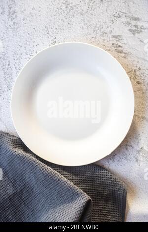 Empty white plate next to a gray kitchen towel Stock Photo