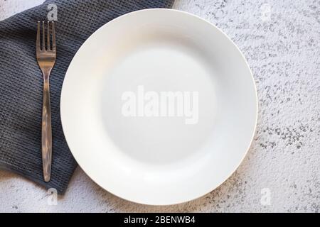 Empty white plate next to a gray kitchen towel Stock Photo