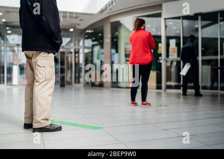 People standing in line front of bank/store due to coronavirus pandemic safety guideline.COVID-19 safe social distancing practice.Quarantine financial Stock Photo