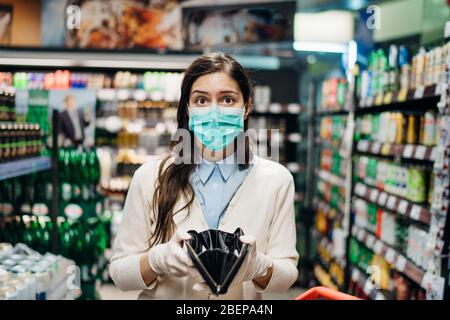 Stressed woman with mask shopping in grocery store with an empty wallet.Bankruptcy/recession.Covid-19 quarantine lockdown impact.Unemployed person in Stock Photo