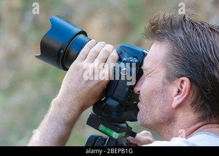Photographer working with a DSLR camera.  He is using a Nikon D800 with a Nikkor 24-70mm F2.8 lens stabilized on a Manfotto tripod head. Stock Photo