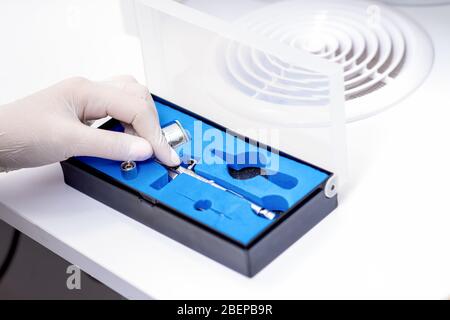 Manicure master hand is taking out airbrush tool for nails wearing white gloves from the box. Stock Photo