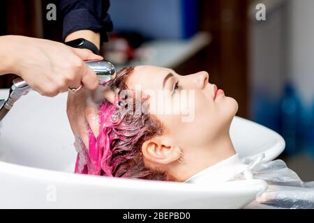 Hairdresser hands washing pink dyed hair of woman in sink, close up. Stock Photo