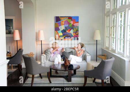 Two women enjoy a drink at lunchtime in a luxury hotel in Cape town. The room is furnished to a high standard of comfort which is common in the city. The white community has created world class hospitality in the country and this has created numerous jobs for all ethnic groups. Stock Photo