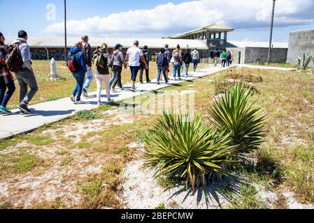 Tourists file across a courtyard in the prison. They are on a tour led by a guide who is a former political prisoner on the island. Stock Photo