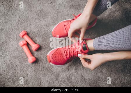 Close up of female hands tying laces on sporty sneakers. Young girl taking break from workout. Concept of fitness and healthy lifestyle. Stock Photo